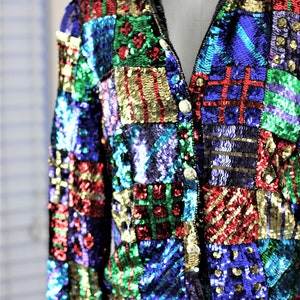Puede incluir: Chaqueta de lentejuelas colorida con dise&ntilde;o de patchwork. La chaqueta presenta una variedad de colores, incluyendo rojo, verde, azul y dorado. Tiene cierre de cremallera y botones dorados. La chaqueta se muestra en un maniqu&iacute;.