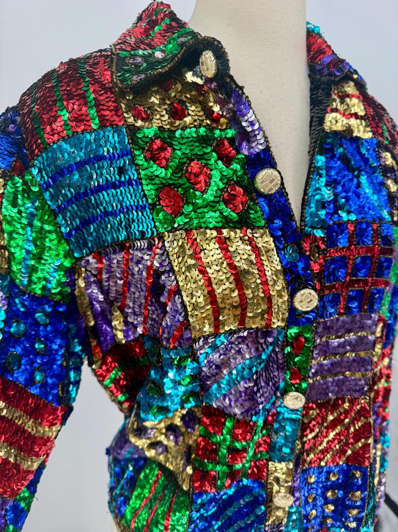 Puede incluir: Chaqueta de lentejuelas colorida con dise&ntilde;o de patchwork. La chaqueta presenta una variedad de colores, incluyendo rojo, verde, azul, dorado y morado. Tiene botones dorados y cuello. Las lentejuelas crean un efecto texturizado y llamativo.
