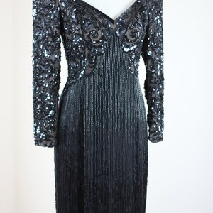 May include: A long-sleeved black sequined dress with a V-neckline. The dress has a fitted bodice and a flowing skirt. The sequins are arranged in a pattern that creates a shimmering effect.
