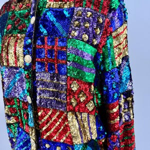 Puede incluir: Una colorida chaqueta de lentejuelas con dise&ntilde;o de patchwork. La chaqueta presenta una variedad de colores, incluyendo rojo, azul, verde, dorado y morado. Las lentejuelas est&aacute;n dispuestas en un patr&oacute;n geom&eacute;trico, creando un aspecto texturizado y llamativo. La chaqueta tiene cuello y botones.
