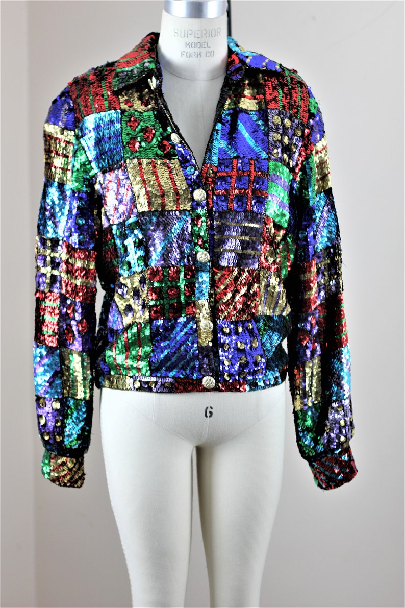 May include: A multi-colored sequined jacket with a patchwork design. The jacket has a button-up front and long sleeves. The sequins are in shades of red, green, blue, gold, and purple.