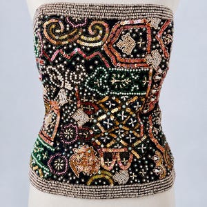 May include: A strapless black corset top featuring intricate hand-beaded and sequined patterns in shades of gold, green, pink, and white. The garment is finished with a dense border of small, uniform beads along the top and bottom edges.