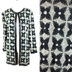 May include: A long, black and silver cardigan with a floral pattern. The cardigan has a satin trim and is made of a sparkly fabric.