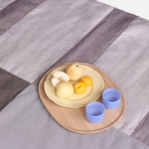 May include: A wooden tray with a yellow plate of fruit and two blue cups. The fruit includes pears and small yellow fruits. The tray is on a gray and brown striped fabric.