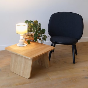 May include: A wooden square side table with rounded edges and a black upholstered chair with a rounded back. A white lamp with a white shade is on the table.