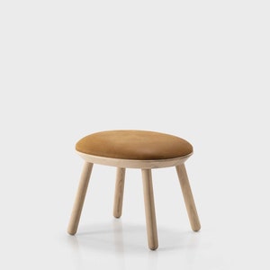 Puede incluir: Un taburete tapizado marrón con la parte superior redondeada y cuatro patas de madera.