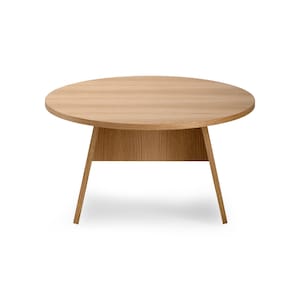May include: A round wooden table with a light brown finish and a simple design. The table has a wide, flat top and four legs that taper towards the bottom.