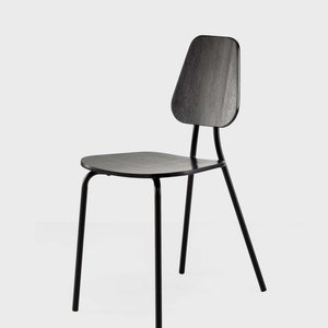 Puede incluir: Silla de madera negra con respaldo curvo y asiento cuadrado. La silla tiene un diseño minimalista con finas patas de metal negro. El respaldo tiene una forma única, añadiendo un toque moderno al mobiliario.