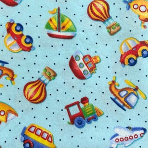 May include: A blue fabric with a white polka dot pattern features various colorful cartoon vehicles, including a sailboat, hot air balloon, airplane, train, car, helicopter, and a boat.
