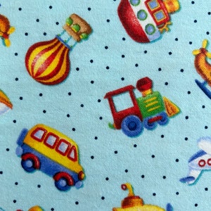 May include: A blue fabric with a white polka dot pattern featuring various colorful cartoon vehicles including a red boat, a yellow submarine, a red train, a yellow school bus, a hot air balloon, and a blue airplane.