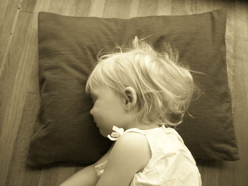 May include: A young child with blonde hair is sleeping on a brown pillow. The child is wearing a white sleeveless shirt.