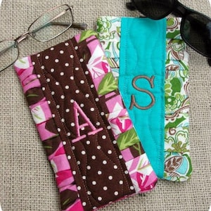May include: Two quilted eyeglass cases with floral fabric and embroidered initials. The case on the left is brown with white polka dots and the initial "A". The case on the right is turquoise with the initial "S".