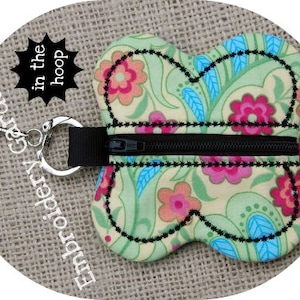 May include: A green, blue, and pink butterfly-shaped zipper pouch with a black zipper. The pouch is attached to a silver key ring with the text "Embroidery Garden in the hoop".