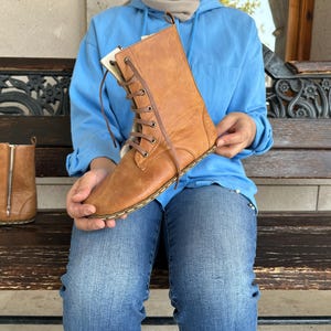 May include: A pair of brown leather boots with a lace-up design and a side zipper. The boots are a light brown color and appear to be new. The boots are approximately 10 inches tall.