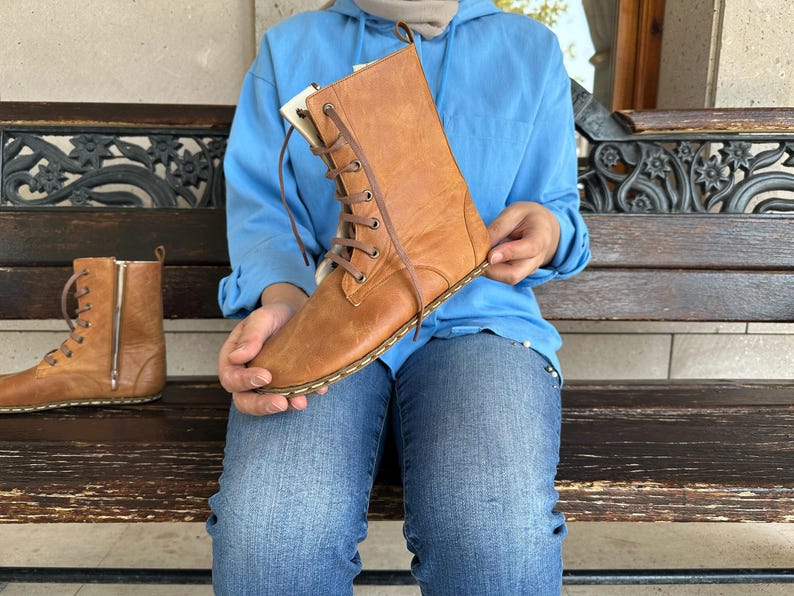 May include: A pair of brown leather boots with a lace-up design and a side zipper. The boots are a light brown color and appear to be new. The boots are approximately 10 inches tall.