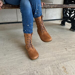 May include: A pair of brown leather boots with a lace-up design. The boots are mid-calf height and have a rounded toe. The image also shows blue jeans with pearl embellishments.