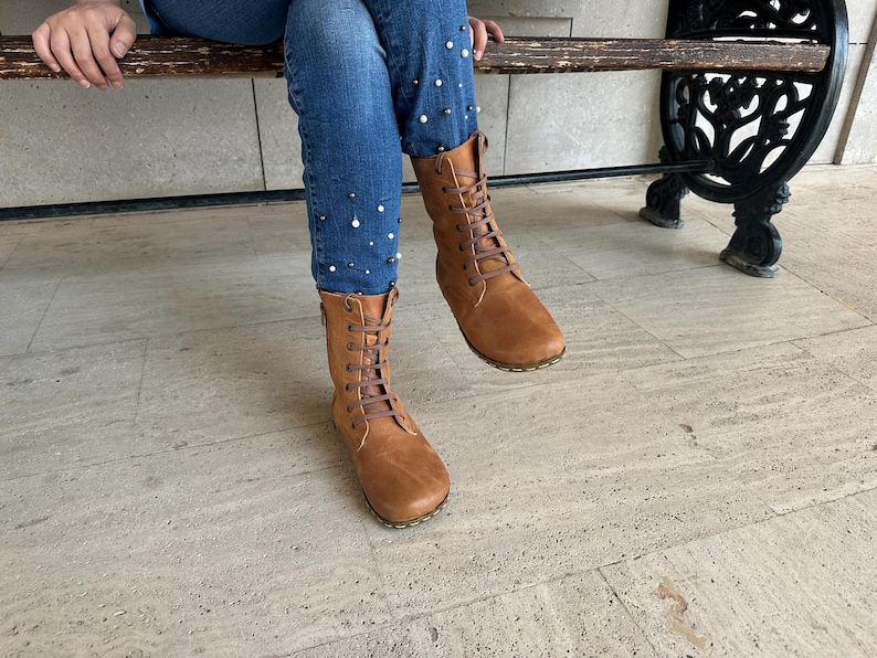 May include: A pair of brown leather boots with a lace-up design. The boots are mid-calf height and have a rounded toe. The image also shows blue jeans with pearl embellishments.