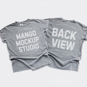 May include: Two gray t-shirts with rolled sleeves. The front shirt displays "MANGO MOCKUP STUDIO" in white text, while the back shirt reads "BACK VIEW." Both shirts have additional text, including "INCLUDES FRONT & BACK" and "COMFORT COLORS 177 GREY."