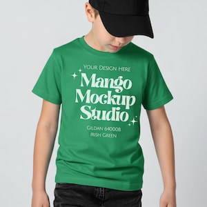 May include: A green t-shirt with the text "Mango Mockup Studio" in white. The shirt is a Gildan 64000B in Irish Green. The person in the image is wearing a black baseball cap and dark jeans.