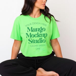 Könnte beinhalten: Ein limettengrünes Gildan 64000 T-Shirt mit dem Text "YOUR DESIGN HERE Mango Mockup Studio LIME" in Grün. Das Model trägt eine schwarze Jogginghose. Das T-Shirt hat einen Rundhalsausschnitt.