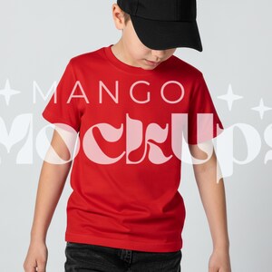 May include: A red t-shirt with the text "MANGO Mockups" in a white, stylized font. The person in the image is wearing a black baseball cap and dark jeans. The shirt is a solid, bright red colour.