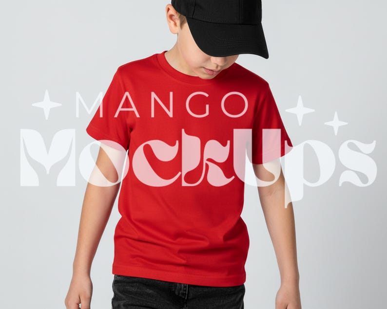 May include: A red t-shirt with the text "MANGO Mockups" in a white, stylized font. The person in the image is wearing a black baseball cap and dark jeans. The shirt is a solid, bright red colour.