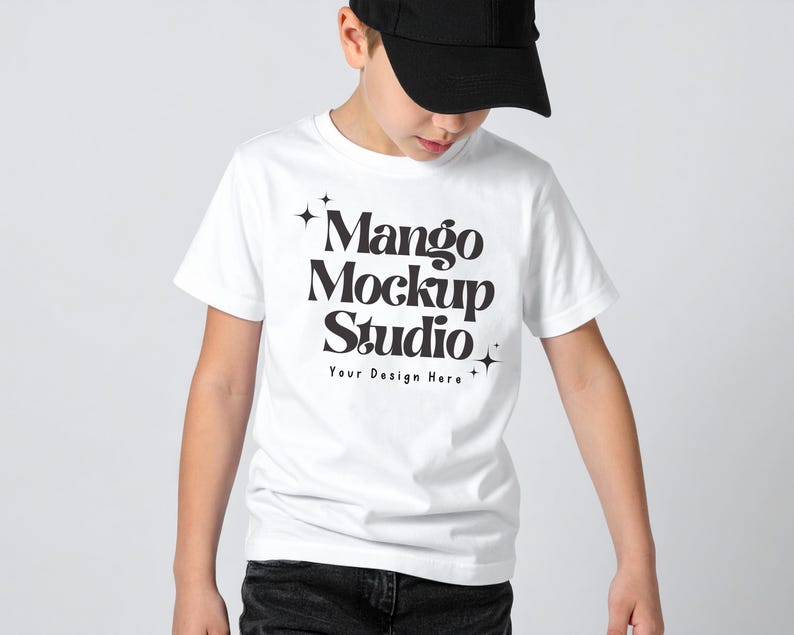 May include: A white t-shirt with the text "Mango Mockup Studio" in a bold, black font. The shirt is worn by a person wearing a black baseball cap and dark jeans. The text "Your Design Here" is below the main text.