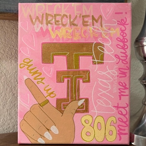 May include: A rectangular pink canvas painting featuring a gold Texas Tech logo, a hand making the guns up gesture, and the text WRECK'EM, Texas Tech University, 806, and meet me in Lubbock! The design includes white heart outlines and gold accents.