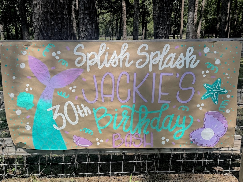 May include: A brown banner with the words "Splish Splash Jackie's 30th Birthday Bash" in white, purple, and teal. The banner features mermaid tail, seashell, and starfish illustrations.