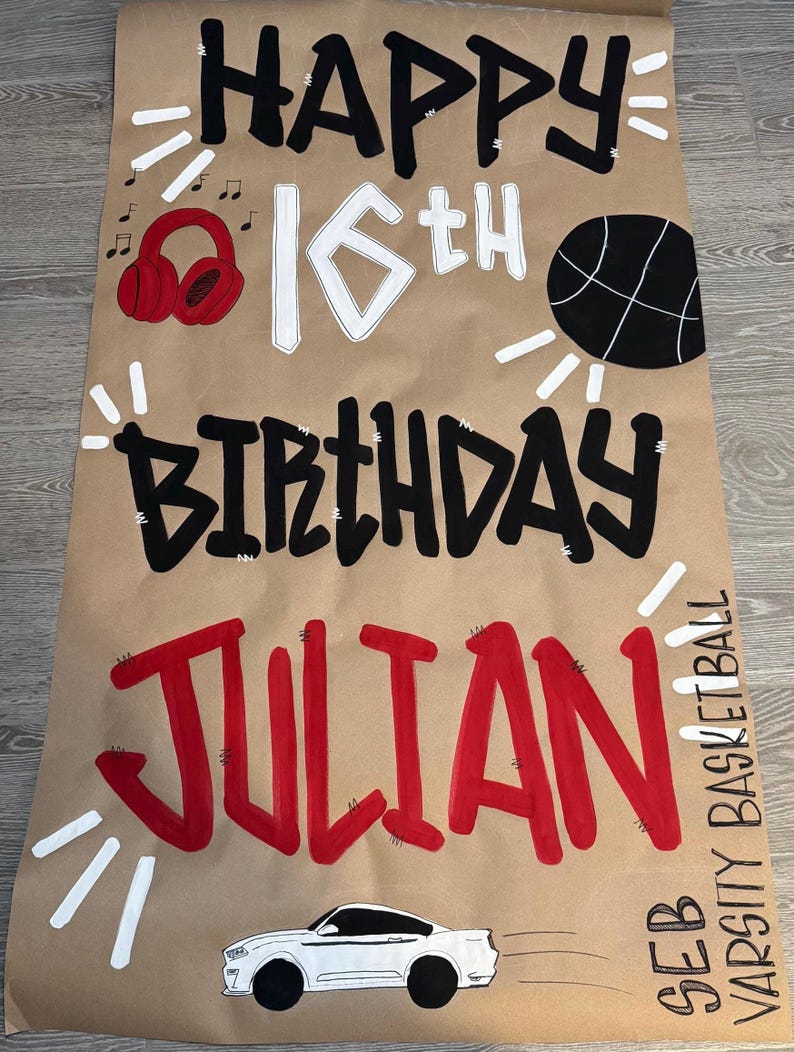 May include: A brown paper birthday banner with the words "HAPPY 16th BIRTHDAY JULIAN" in black and red lettering. The banner includes a basketball, headphones, a car, and the text "SEB VARSITY BASKETBALL".