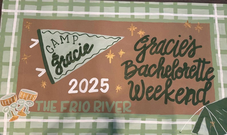 May include: A hand-painted banner with a brown background and a green and white checkered border. The banner reads "Camp Gracie" and "Gracie's Bachelorette Weekend 2025 The Frio River" in a whimsical font. Decorative elements include stars, drums, and a tent.