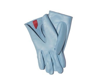 May include: A pair of light blue leather gloves featuring a V-shaped cutout at the wrist and a small, contrasting red tab detail on the interior lining. The gloves have a smooth finish and are positioned overlapping each other on a plain surface.