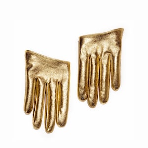 May include: Two gold-colored, hand-shaped gloves. The gloves are made of a shiny, metallic material. The fingers are clearly defined, and the gloves appear to be small, possibly for a child or as a decorative item.