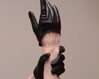 May include: Black leather gloves with a classic design. The gloves are form-fitting and reach the wrist. The fingers are individually shaped, and the leather has a smooth, polished appearance. The gloves are a solid black color.