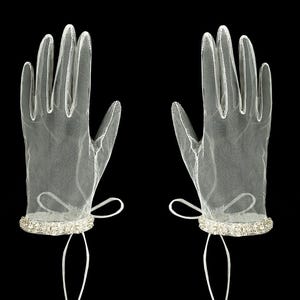 K&ouml;nnte beinhalten: Ein Paar wei&szlig;e T&uuml;llhandschuhe mit Strassbesatz. Die Handschuhe haben eine Schleife am Handgelenk.