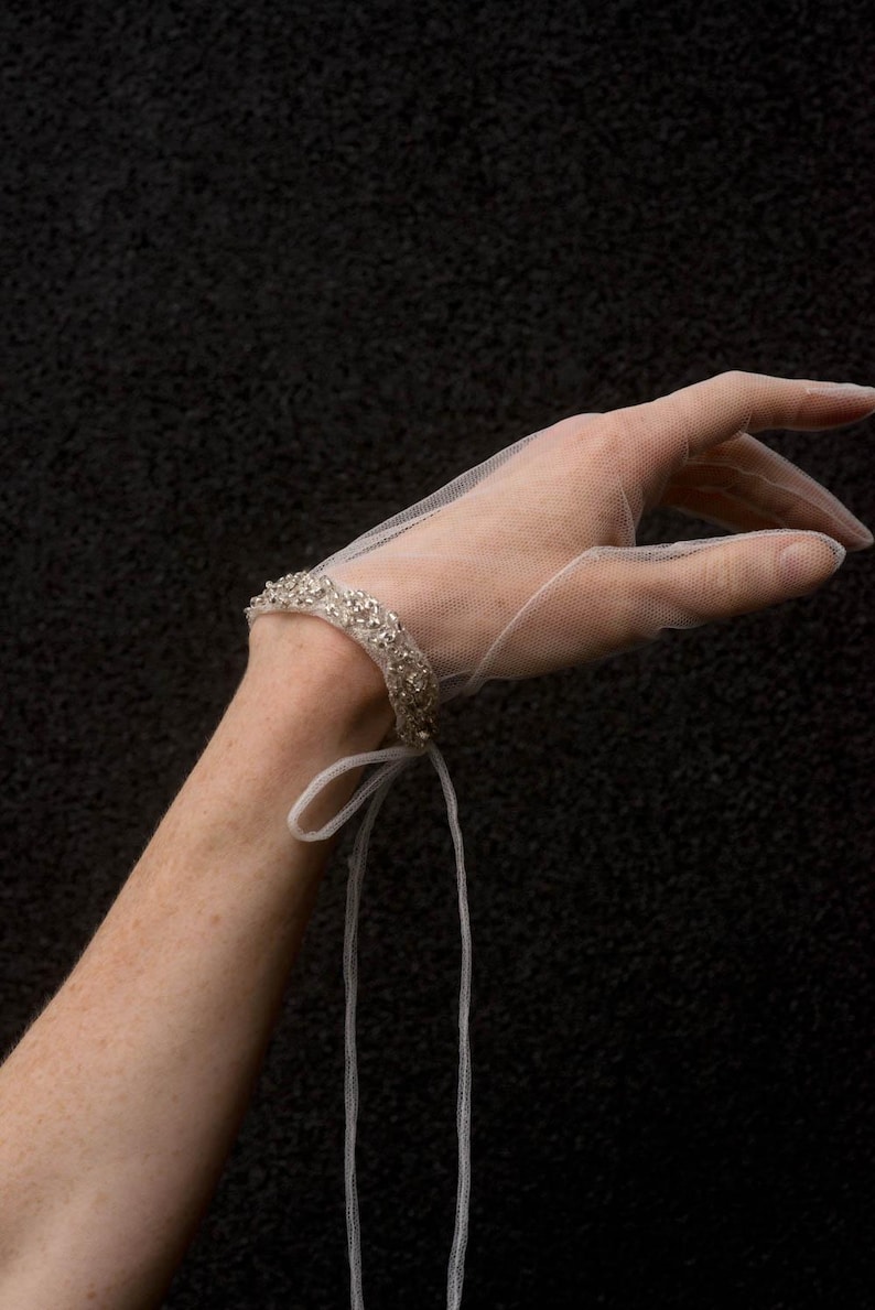 K&ouml;nnte beinhalten: Ein wei&szlig;es T&uuml;ll-Armband mit Perlenbesatz und einer langen wei&szlig;en Schleife.