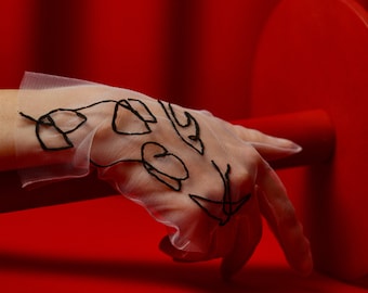May include: A white sheer glove with black embroidered designs on a red background.