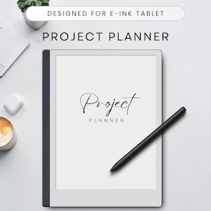 May include: A white e-ink tablet with a black stylus and the text "Project Planner" on the screen. The tablet is on a white surface with a laptop, a cup of coffee, and a small white object.