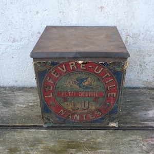Peut inclure: Boîte en métal vintage avec une étiquette rouge, bleue et blanche. L'étiquette indique "Le Fevre Utile Aux Herboristes Petit Beurre LU Nantes".