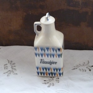 May include: White ceramic vinegar bottle with a blue and orange geometric pattern and the word "Vinaigre" written on the front.