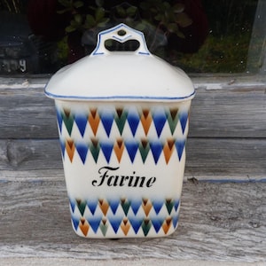 Puede incluir: Un bote de cerámica blanco con tapa y asa. Presenta un patrón geométrico de diamantes azules, naranjas y verdes. La palabra "Farine" está escrita en la parte delantera en escritura negra.