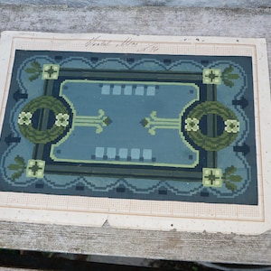 Könnte beinhalten: Ein Vintage-Teppichdesign, das auf Papier mit einem Rastermuster gedruckt ist. Das Design zeigt einen blauen Hintergrund mit grünen und schwarzen geometrischen Formen und einem floralen Motiv.
