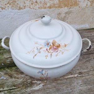 Puede incluir: Plato de cazuela de esmalte blanco con tapa, con un diseño floral con flores azules, rosas y marrones. El plato tiene dos asas a los lados.