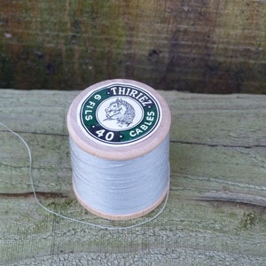 Op de afbeelding: Een spoel grijs garen met een groen label waarop "Thiriez Fils 40 Cables" staat. Het label heeft een paardenkoplogo.