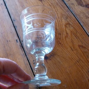 May include: A clear glass goblet with a stemmed base and etched designs. The goblet is on a wooden surface.