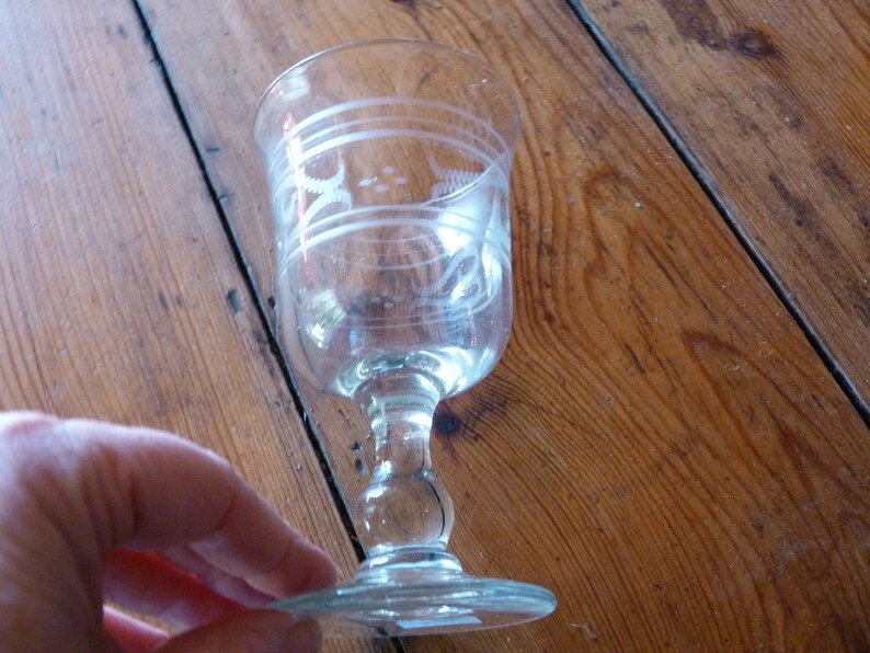 May include: A clear glass goblet with a stemmed base and etched designs. The goblet is on a wooden surface.