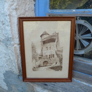 Peut inclure: Une photographie en noir et blanc encadrée d'un bâtiment en pierre avec une tour. Le bâtiment a un toit pointu et plusieurs fenêtres. La photographie est dans un cadre en bois avec une finition brun clair.