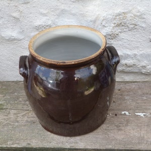 May include: A brown glazed ceramic crock with two handles. The crock is empty and has a white interior.