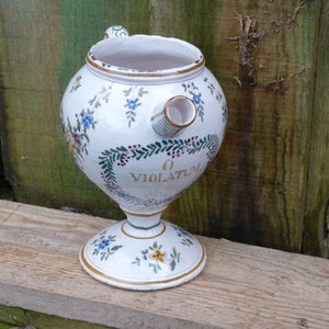 Puede incluir: Jarra de cerámica blanca con un diseño floral y la palabra "VIOLATUM" en letras doradas. La jarra tiene un pico y dos asas.