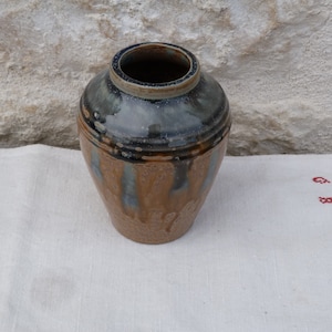 Peut inclure: Un vase en céramique brun avec un glaçage bleu et blanc. Le vase a un corps arrondi et une ouverture étroite.